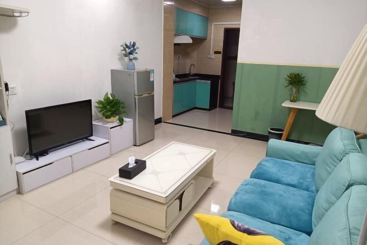 A compact living space with a TV, a small kitchen, and a blue sofa.