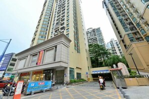 A high-rise building with a commercial ground floor, a pedestrian area with a yellow grid pattern, and a person walking.