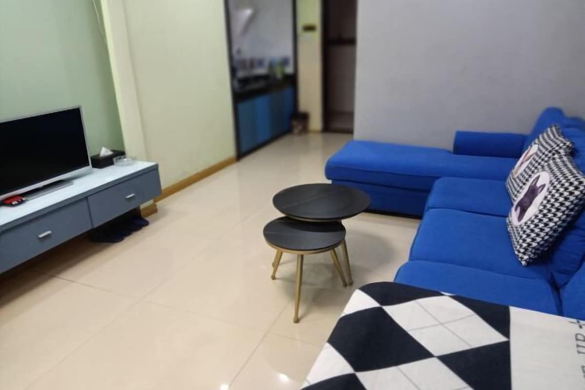 A living room with a sofa, a television, a small table, and a patterned cushion.