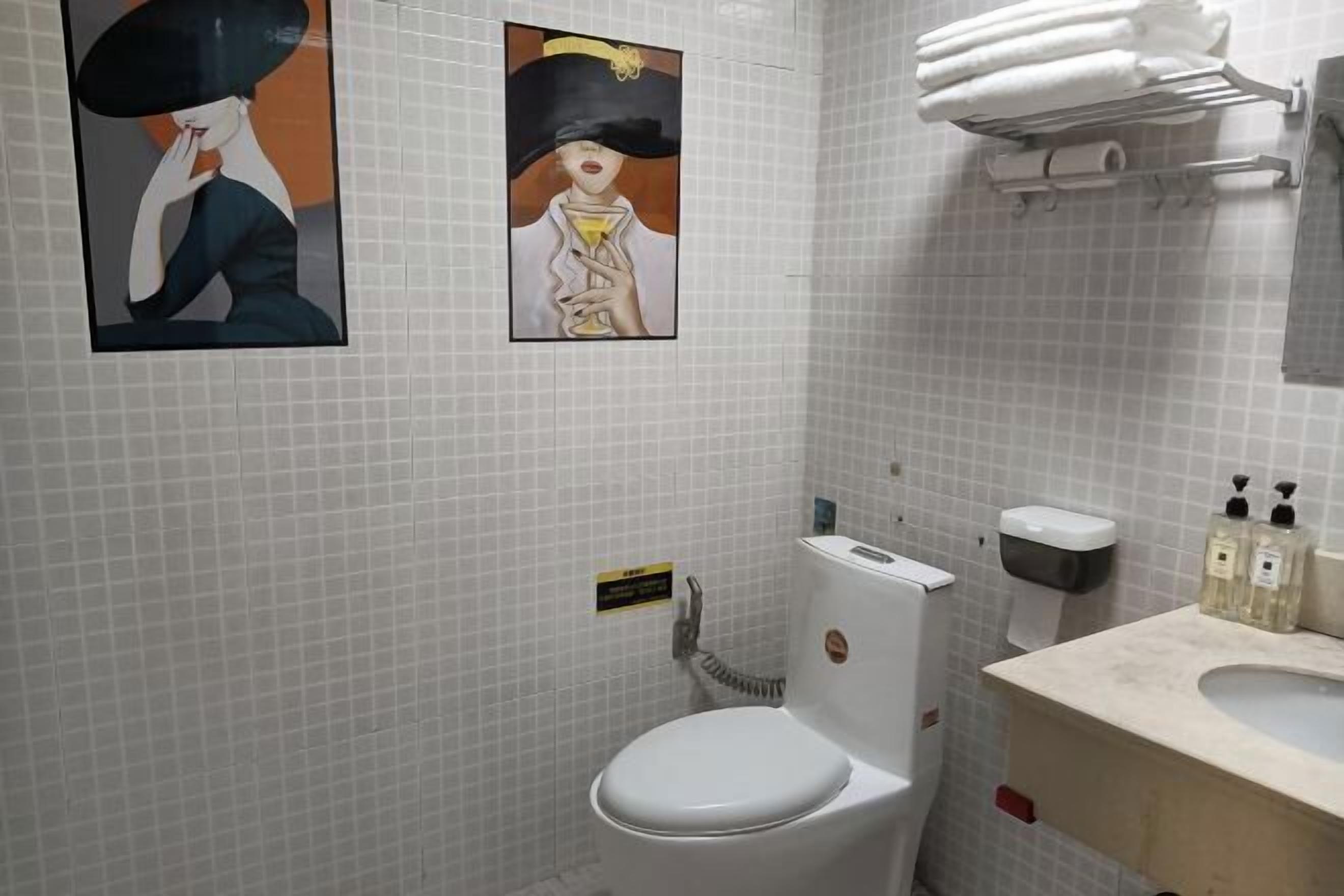 Un baño con inodoro blanco, un perchero con toallas dobladas, un dispensador de jabón y dos cuadros en la pared.