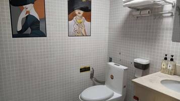 Un baño con inodoro blanco, un perchero con toallas dobladas, un dispensador de jabón y dos cuadros en la pared.