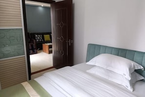 A hotel room with a bed, a wardrobe, and a door leading to another room.