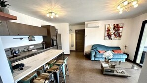 Una cocina moderna con barra, una sala de estar con sofá y una mesa de centro, y un ventanal grande.