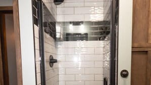 A modern bathroom with white subway tiles, a glass shower enclosure, and a wooden door.
