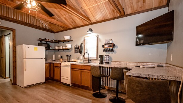 A kitchen with wooden cabinets, a refrigerator, a stove, and bar stools.