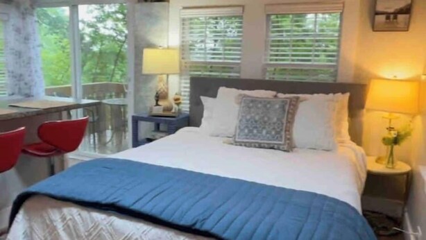 Ein Schlafzimmer mit einem Bett, zwei Nachttischen, einem Schreibtisch mit Stuhl und Fenstern mit Jalousien.
