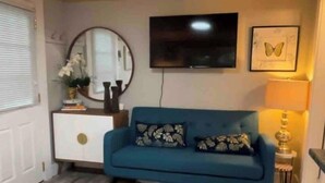 Ein Wohnzimmer mit einem blauen Sofa, einem an der Wand montierten Fernseher, einem runden Spiegel und einem gerahmten Bild.