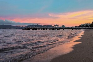 A coastal scene with a pier extending into the water, a beach, and buildings in the background. - Cape No. 7 Sea House (Shenzhen)