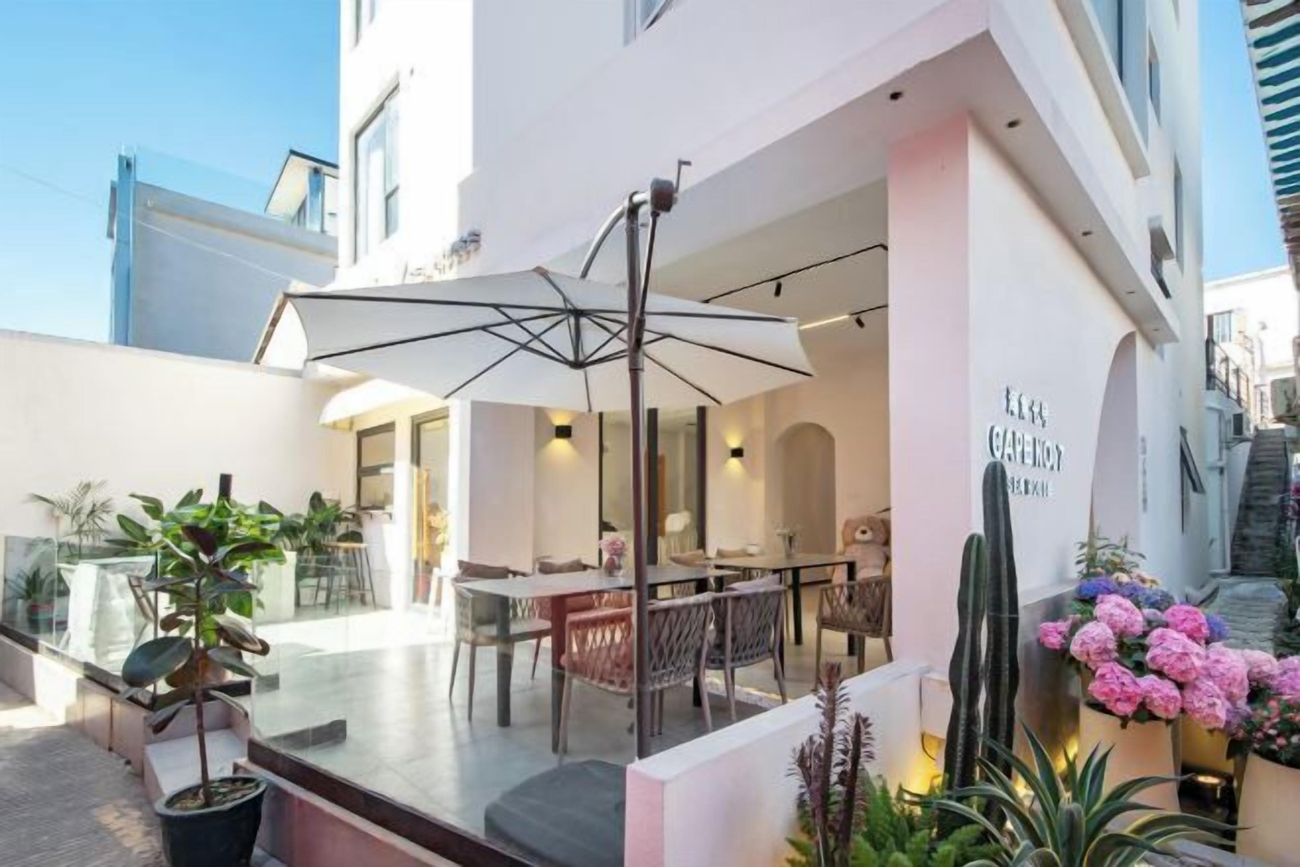Un área de comedor exterior moderna con mesa, sillas, una sombrilla grande y plantas en macetas.