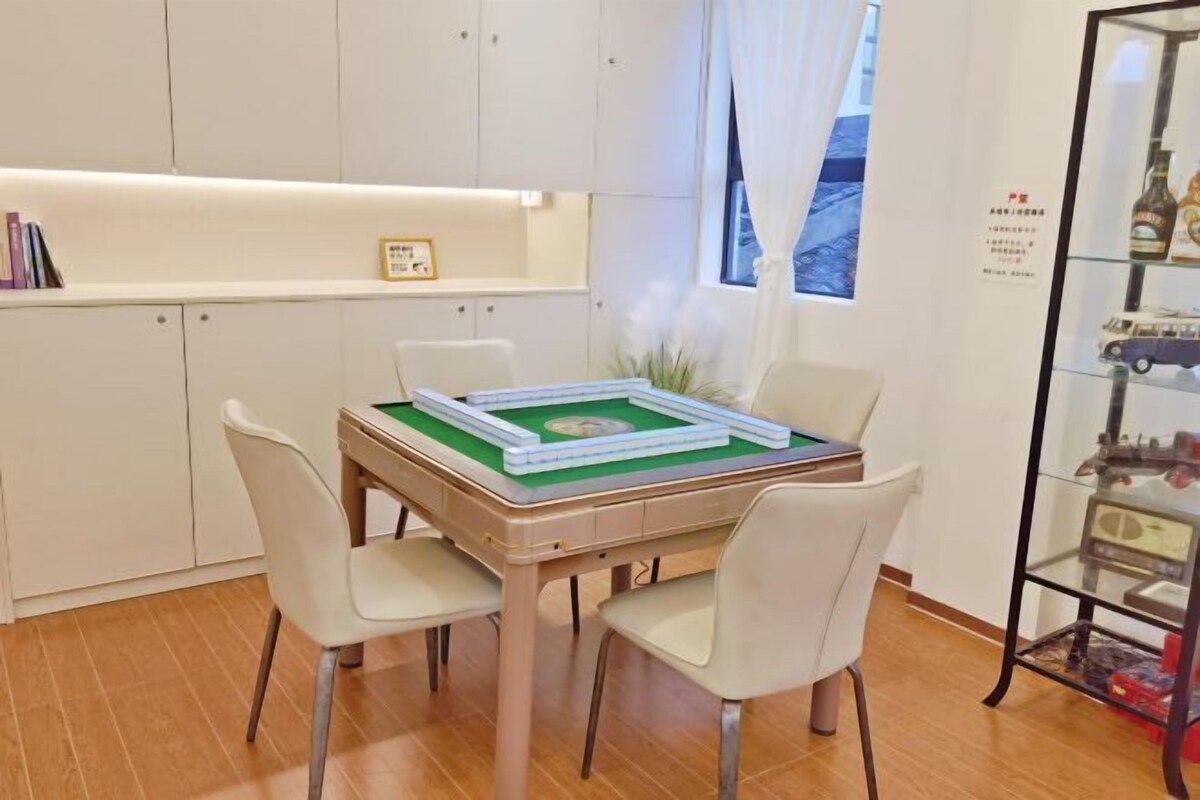 A dining area with a table set for two, a bookshelf, and a window with curtains.