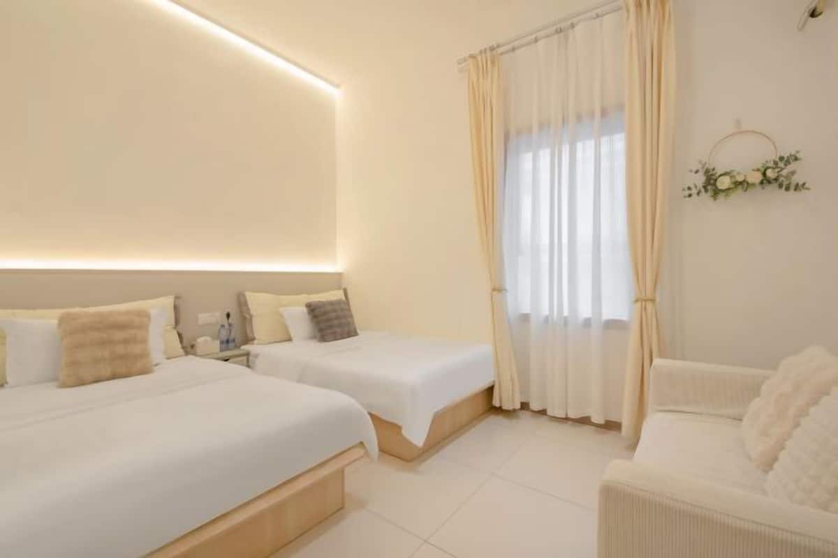 Habitación de hotel con dos camas, un sofá y un ventanal grande con cortinas.