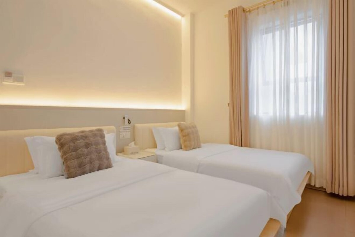 A hotel room with two beds, a bedside table, a nightstand, and a window with curtains.