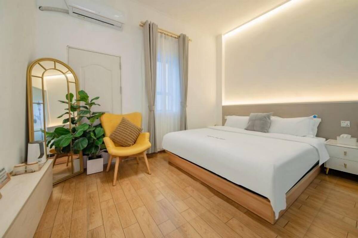 Un dormitorio moderno con una cama grande, una mesita de noche, una silla, un espejo y una planta en maceta.