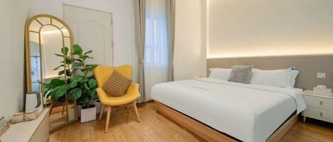 A modern bedroom with a large bed, a bedside table, a chair, a mirror, and a potted plant.