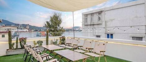 A rooftop terrace with a table and chairs, a canopy, and a view of buildings and mountains.