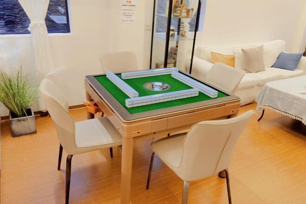 A room with a green felt table for board games, white chairs, a white sofa, and a small potted plant.