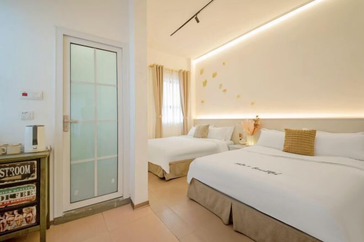 A hotel room with two beds, a bedside table, a nightstand, a wall-mounted light, and a door with frosted glass panels.