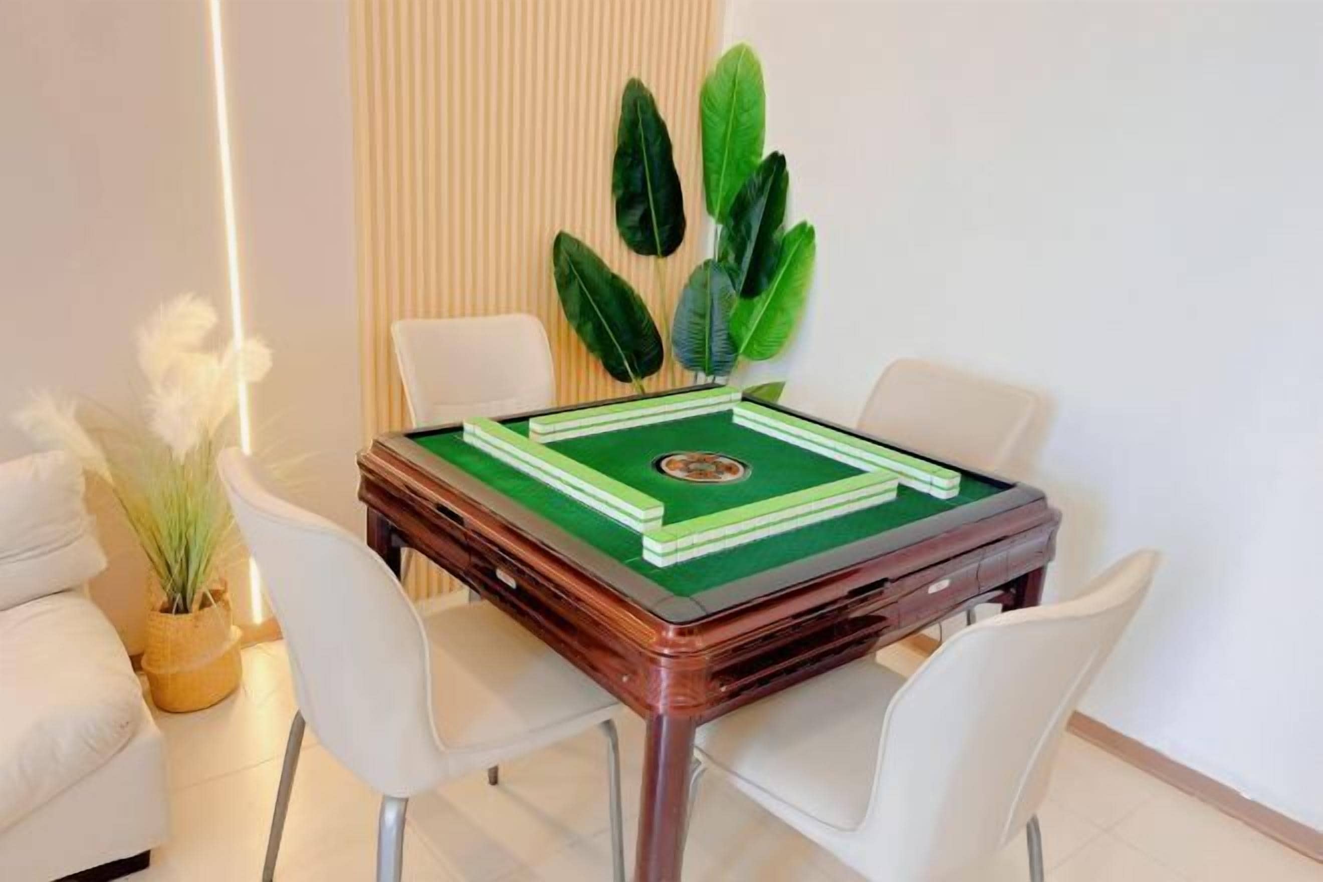 A room with a green pool table, white chairs, and a potted plant.
