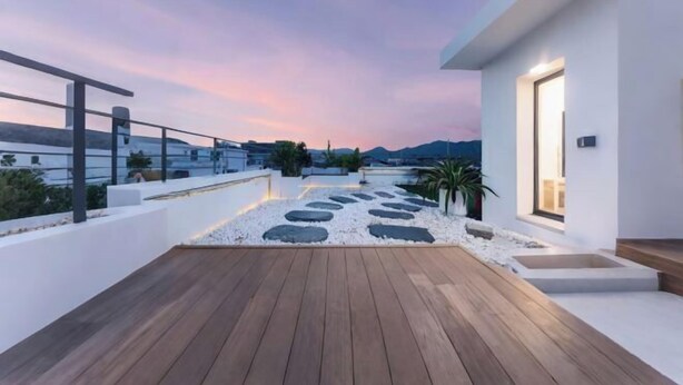 Une terrasse moderne sur le toit, dotée d’une plateforme en bois, de murs blancs et offrant une vue sur les montagnes lointaines sous un ciel crépusculaire.