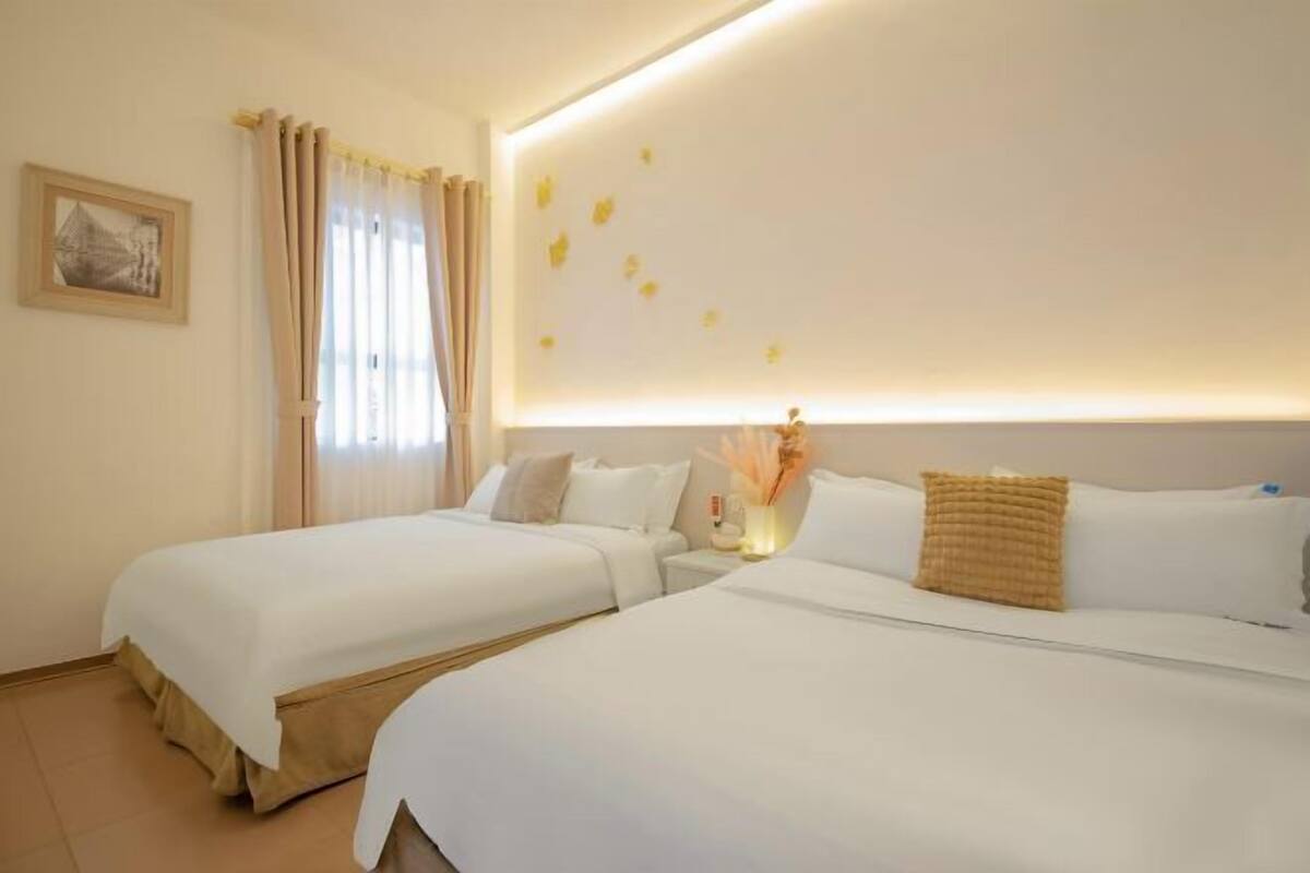 Habitación de hotel con dos camas, una mesita de noche con lámpara y una lámpara de pared.