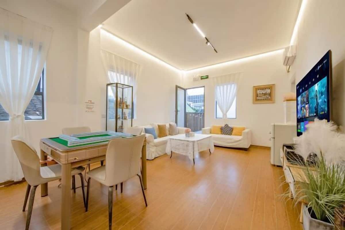 Habitación de hotel moderna con zona de comedor, un conjunto de sofás, televisión de pantalla plana y una planta en maceta.