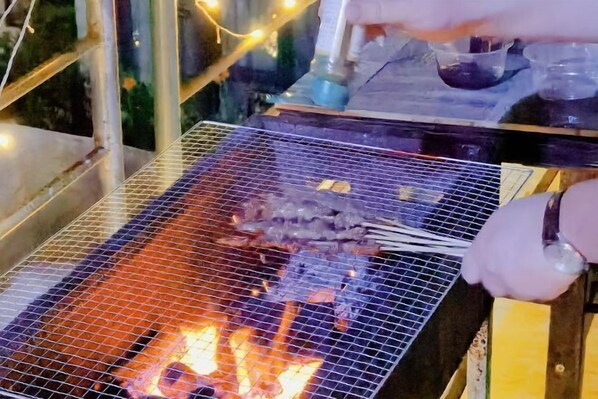 A grill with food being cooked over an open flame. - Cape No. 7 Sea House (Shenzhen)