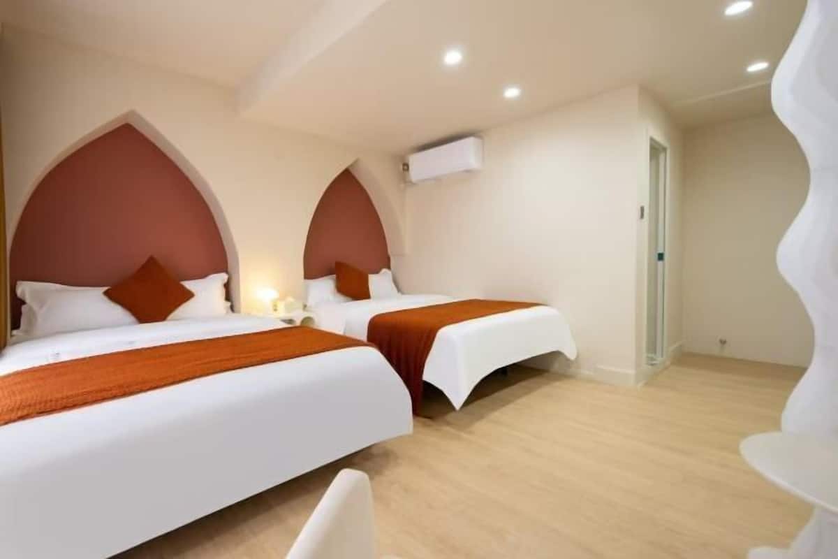 Habitación de hotel con dos camas, techo blanco y suelo de madera.