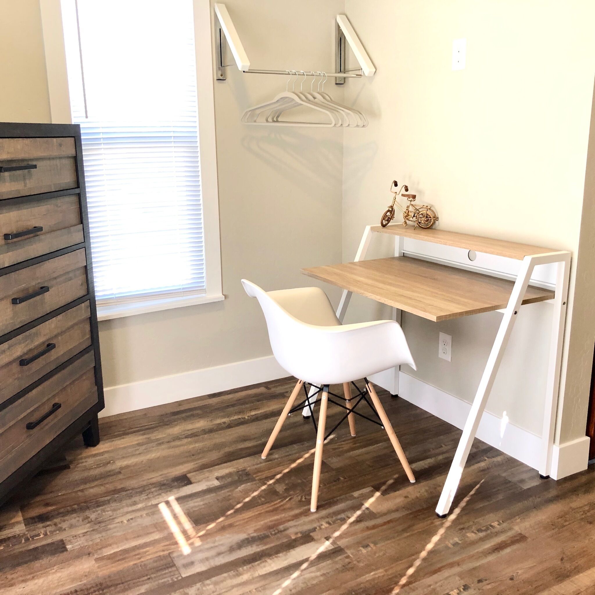 A room with a wooden desk, white chair, and a dresser.