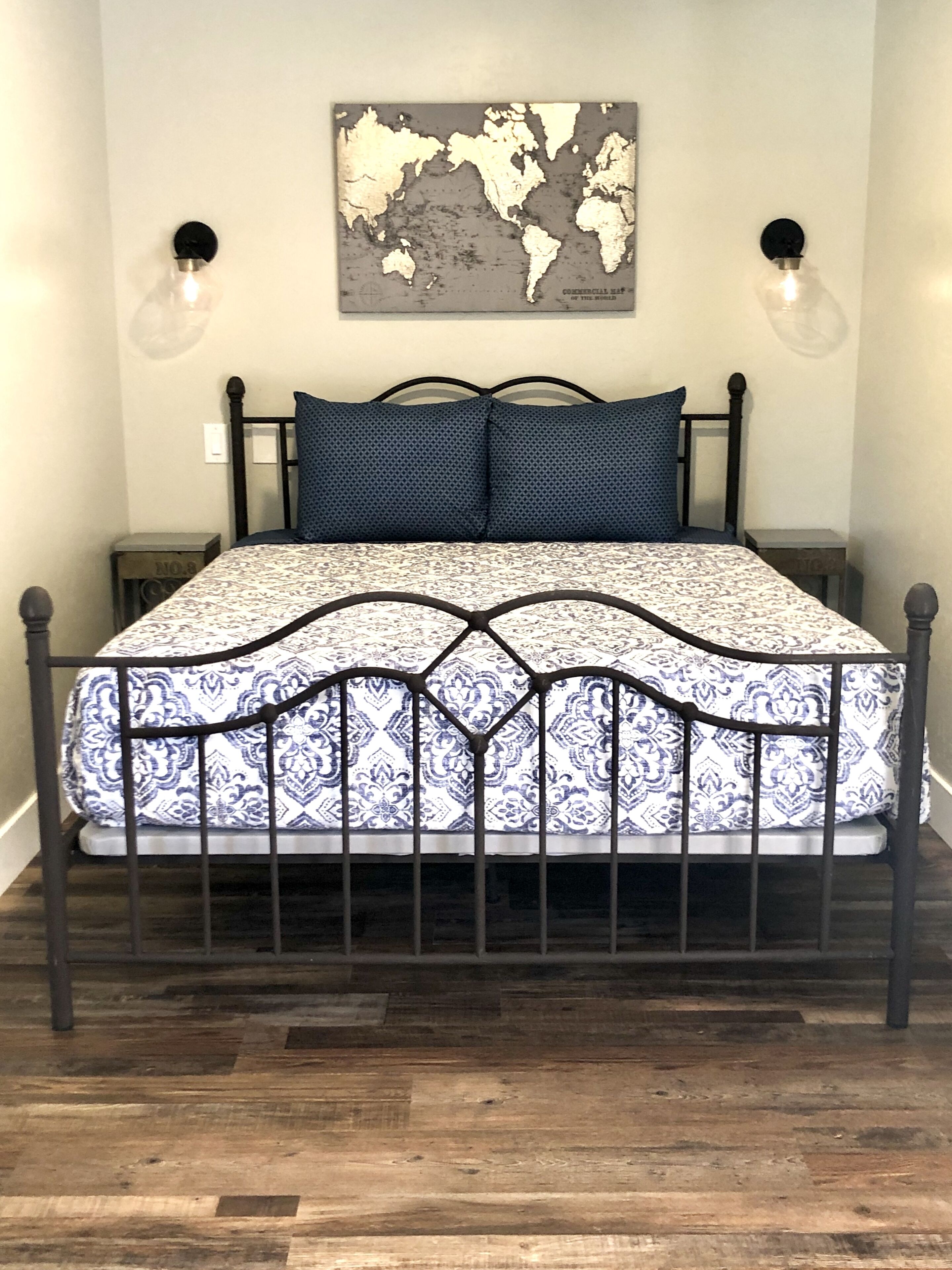 Una cama con una colcha estampada, un mapa del mundo en la pared y dos lámparas de pared.