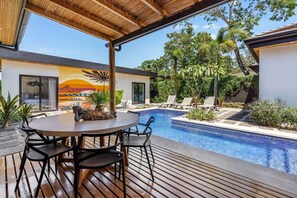 A poolside area with a wooden deck, a round table with chairs, and a mural on the wall.