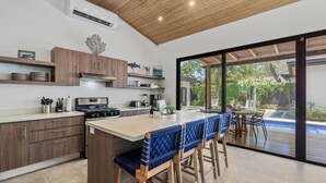 Une cuisine moderne dotée d’un îlot central, de meubles en bois et d’une grande porte-fenêtre coulissante donnant sur un espace extérieur.
