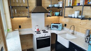 Cocina compacta con estufa, horno, microondas, pileta y estantes con vajilla y utensilios.