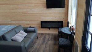 Interior acogedor de una cabaña con pared de madera, televisor de pantalla plana, chimenea, sofá y mesa de comedor.