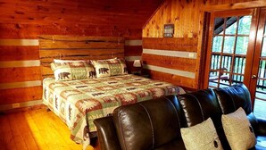 A wooden cabin room with a bed, a leather couch, and a sign indicating it's a cabin. - Cozy Studio Cabin In The Smokies. Close to Pigeon Forge + Wears Valley. (Sevierville)