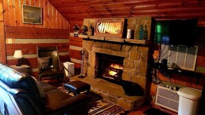 A cozy cabin interior with a stone fireplace, leather sofa, and a television mounted on the wall. - Cozy Studio Cabin In The Smokies. Close to Pigeon Forge + Wears Valley. (Sevierville)