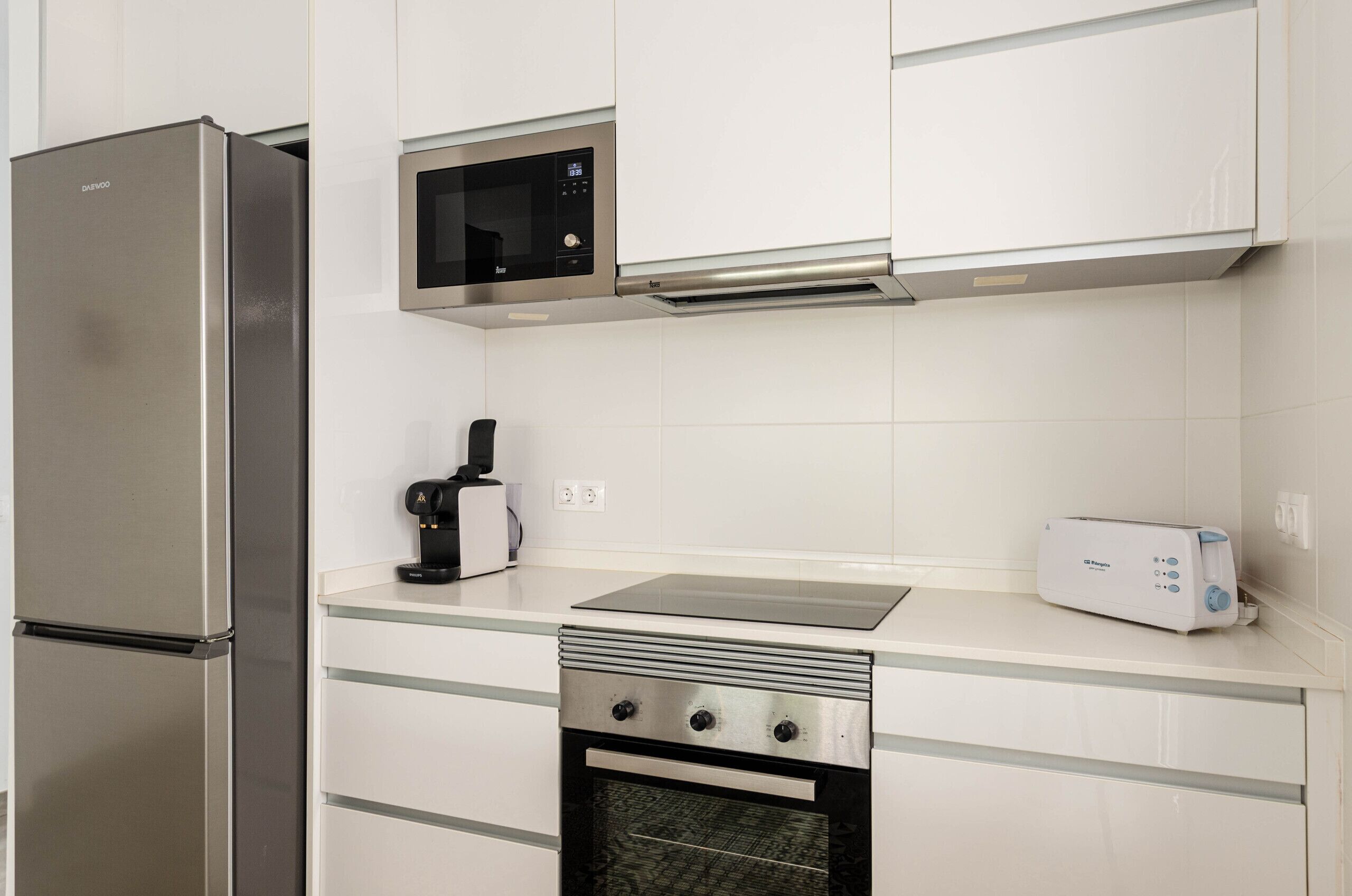 A kitchen with a stainless steel refrigerator, a microwave, a toaster, and a built-in oven.