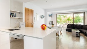 A modern kitchen with a dishwasher, a central island with a fruit bowl, and a dining area with a sofa and a coffee table. - YourHouse Can Cortana (Pollensa)