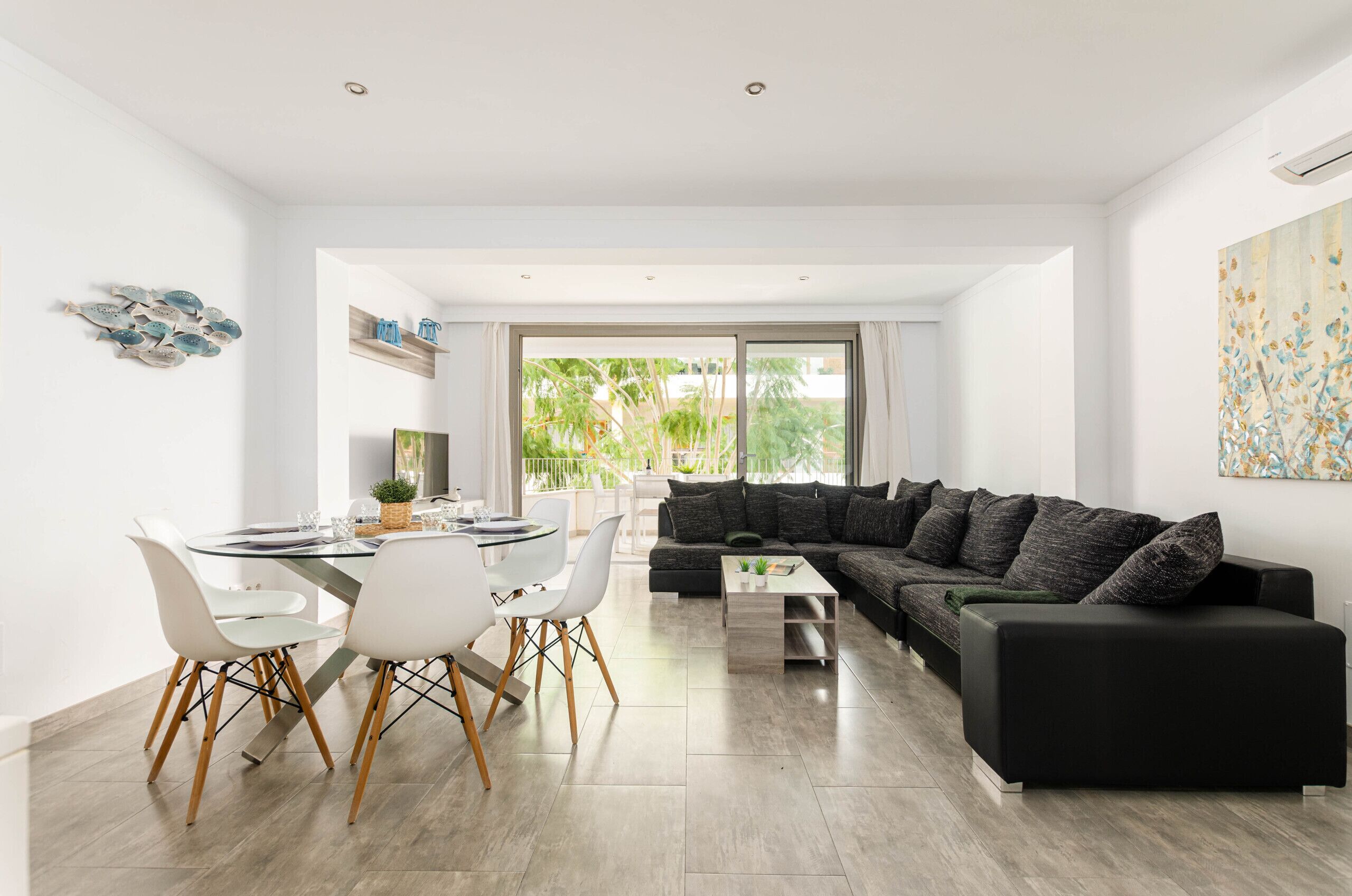 A modern living room with a black sofa, white chairs, and a glass dining table.