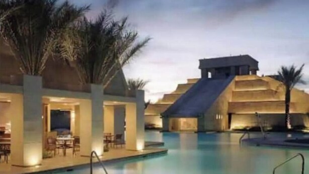 A pool area with a water slide, palm trees, and a building with a flat roof. - Cancun Resort 1 Bedroom LasVegas! (Celebration)