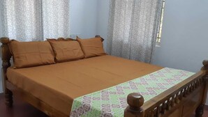 A bed with a wooden frame and brown bedding, curtains, and a patterned table runner. - Villa Le Bonheur Auroville Pondicherry India (Bommayapalayam)