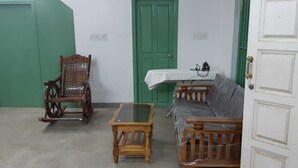 A room with a green door, a wooden rocking chair, a glass-top table, and a sofa. - Villa Le Bonheur Auroville Pondicherry India (Bommayapalayam)