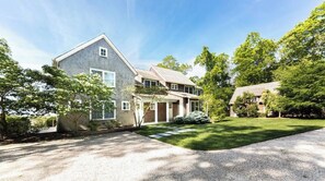 Traditional two-story house with a gabled roof and front porch, set amidst a serene and lawn with mature trees.