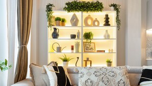 A modern living room with a sofa, a round coffee table with candles, and a decorative shelf with plants and vases. - Luxury Notting Hill Flat with Patio (London)