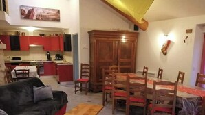Un salon avec un canapé, une table à manger en bois et des chaises, une cuisine à l’arrière-plan et un grand meuble en bois.