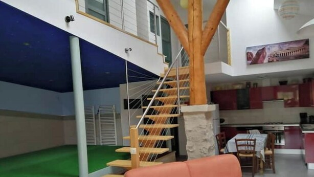 Un intérieur moderne avec un escalier en bois, un espace recouvert de gazon synth étique vert et une cuisine en arrière-plan.