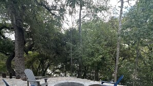 An outdoor seating area with stone flooring, a fire pit, and Adirondack chairs. - Completely renovated 1930s Cottage on the Guadalupe River. Ideal location! (New Braunfels)