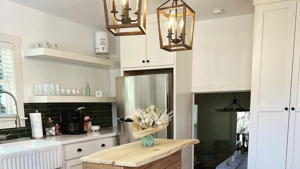 A modern kitchen with a wooden island, bar stools, pendant lights, and white cabinetry. - Completely renovated 1930s Cottage on the Guadalupe River. Ideal location! (New Braunfels)