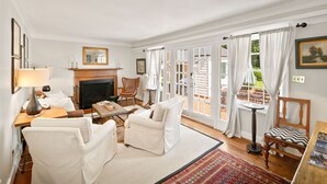 A well-lit living room with a fireplace, white furniture, and a view through large glass doors. - GreenLeaf | Close to UVA and Downtown, Sleeps 7 with Yard! (Charlottesville)