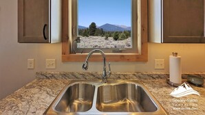 Una cocina con un lavamanos doble, armarios de madera y una ventana que ofrece vistas a un paisaje montañoso.