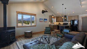 Amplia sala de estar con chimenea, un ventanal con vista a las montañas, cocina equipada con electrodomésticos modernos y un rincón de descanso acogedor.